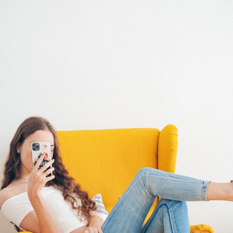 woman in white tank top and blue denim jeans sitting on yellow sofa